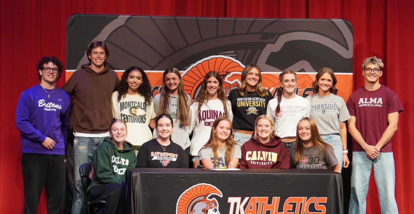 Group of students in athletic gear celebrating college commitments on stage.