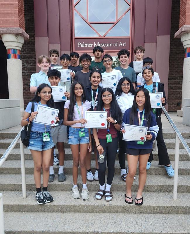 Image of students holding their certificates standing outside the Palmer Museum of Art
