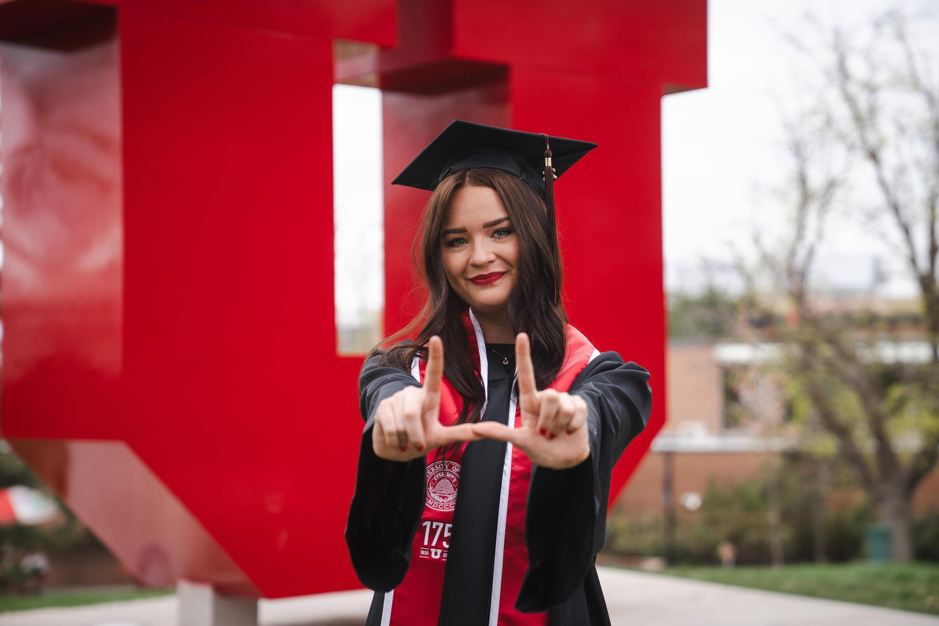 Ms. Carn in graduation regalia, standing in front of the "Block U," a giant, red, U sculpture on the University of Utah campus.