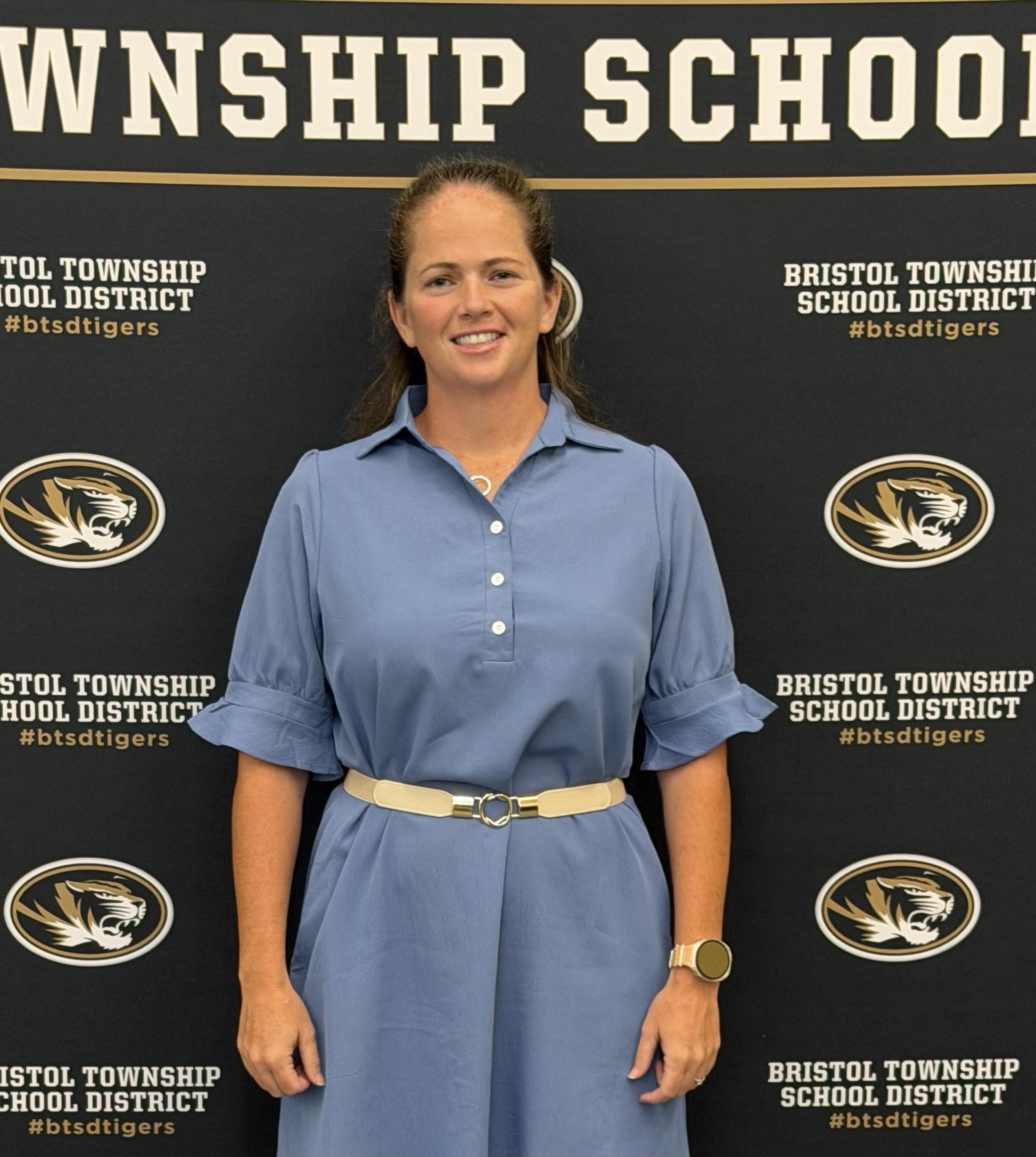 Professional portrait of Kyle Hoffman, smiling and wearing a light blue dress with a cream belt.