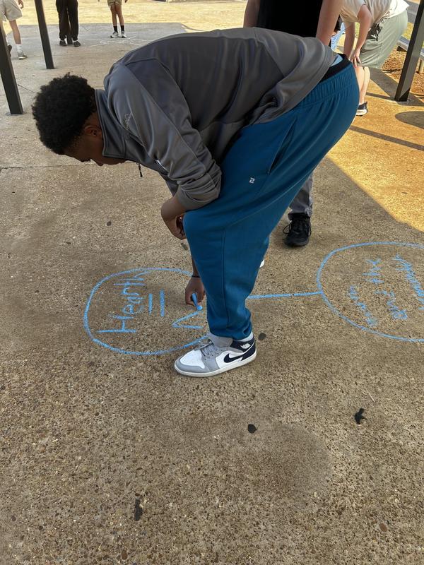 Student writing on concrete outside with blue chalk
