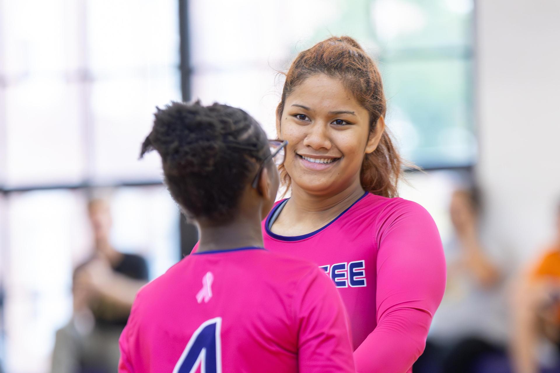 Smiling volleyball players sharing a moment of celebration after a play.