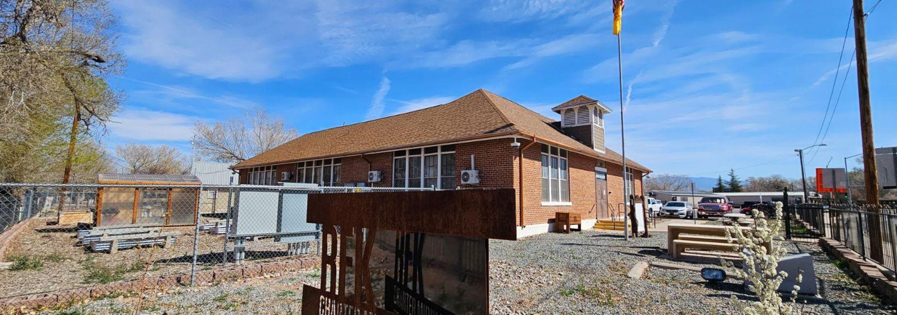 Brick building with a sloped roof, flagpole, and outdoor seating area.