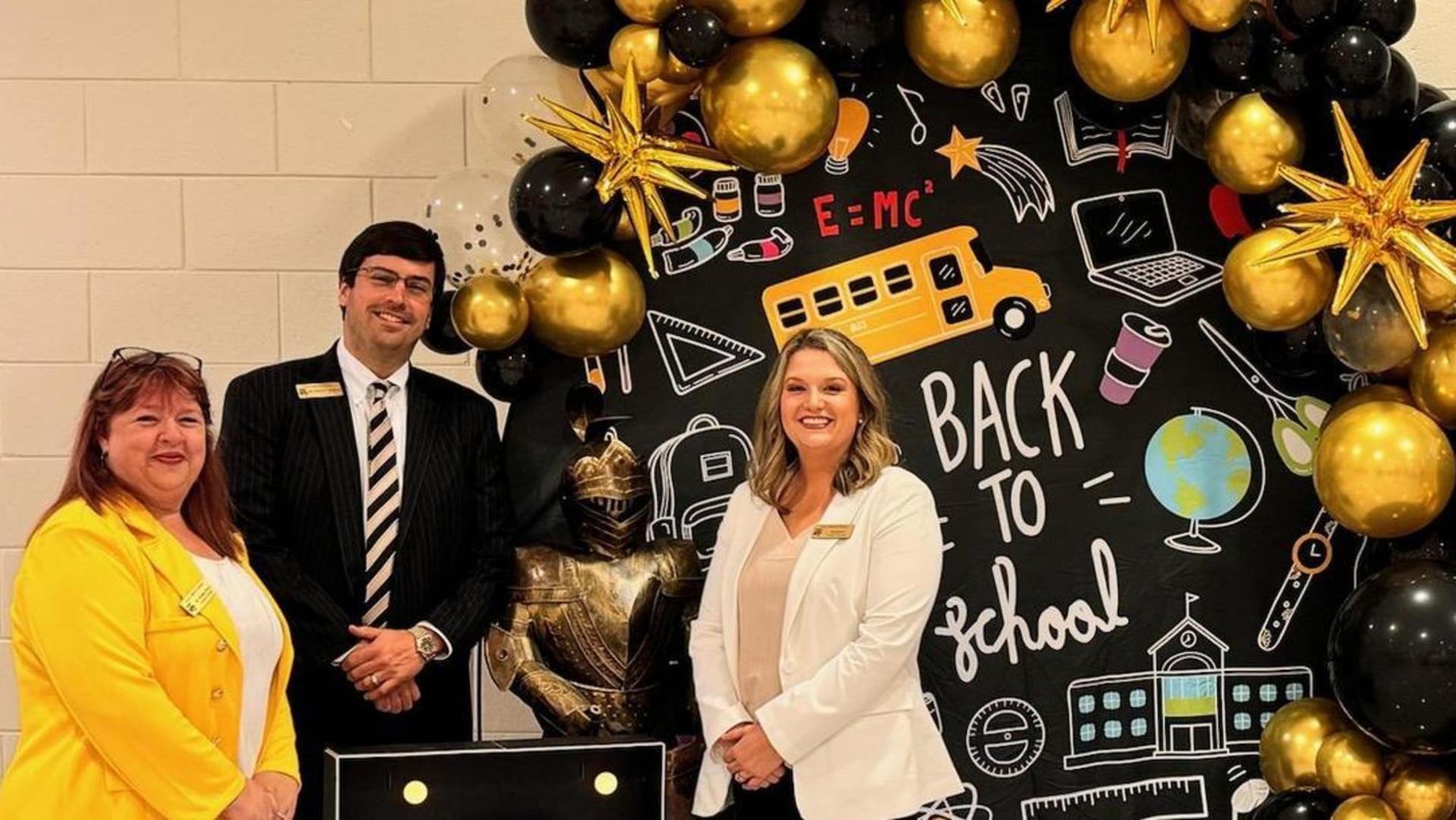 A decorated backdrop for a school event with balloons, stars, and a smiling woman and man.