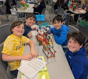 Four male students smile surrounding their K'Nex prototype at the STEM Design Challenge.