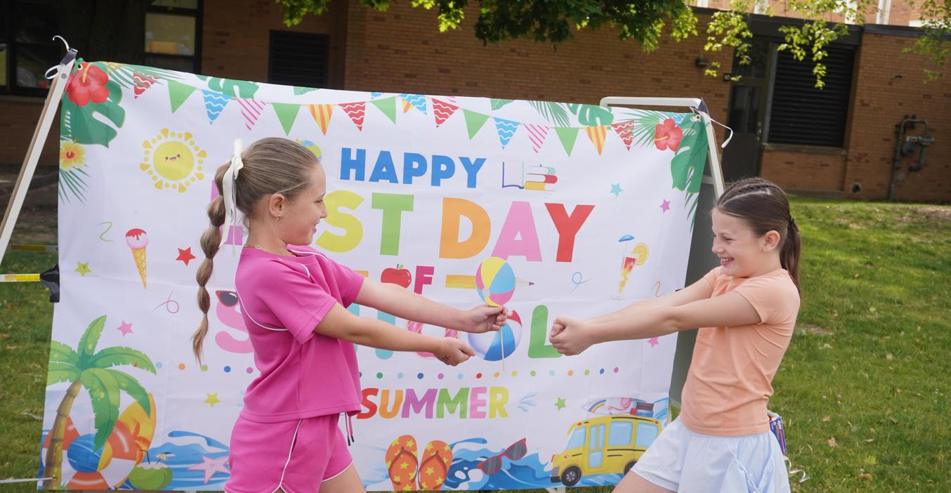 Two children playfully reaching out to each other in front of a colorful banner.