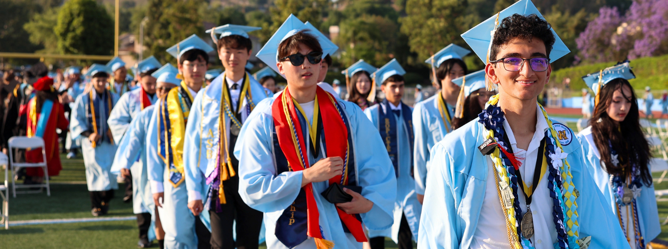 Graduates in light blue robes and caps walking together at a graduation ceremony.