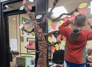 Two students putting leaves on Giving Tree