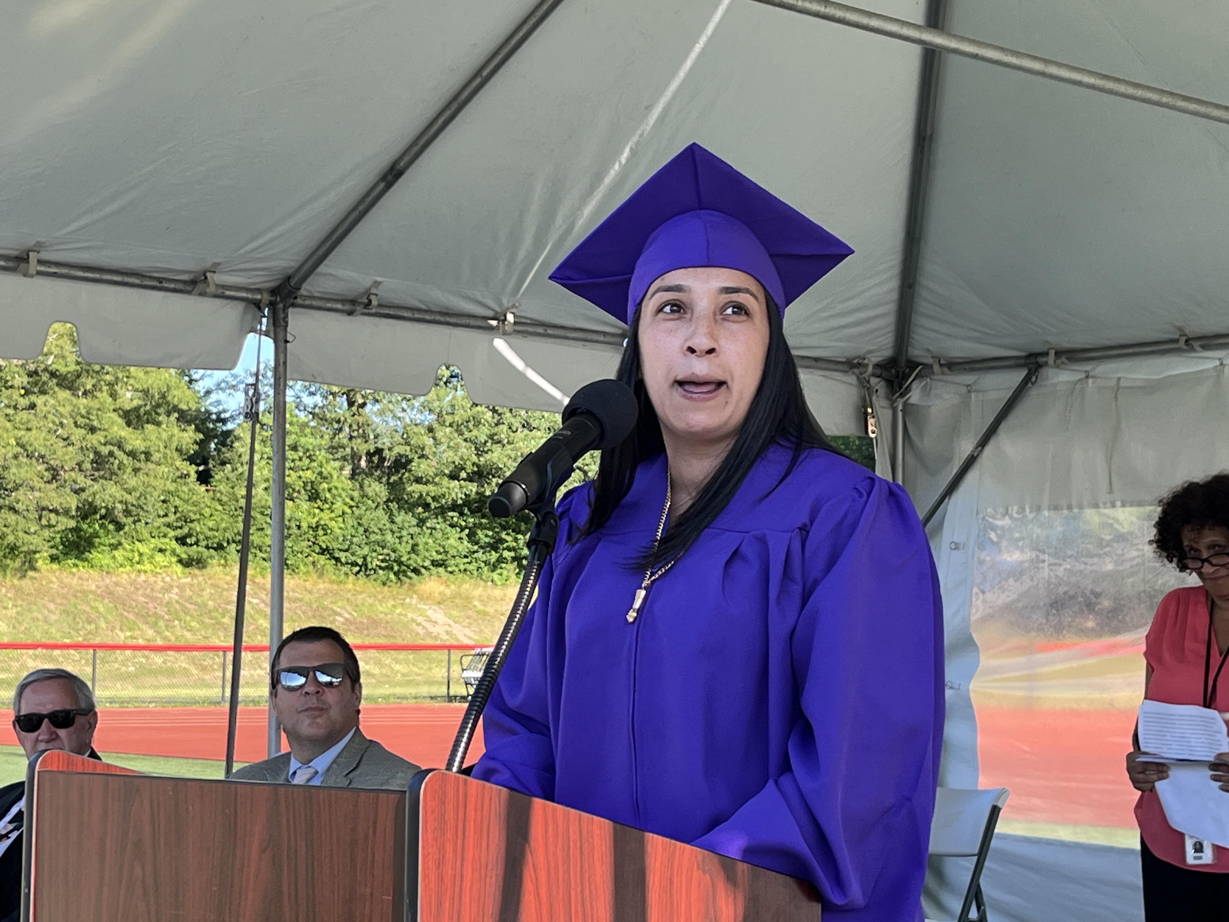 woman in purple cap and gown speaks at graduation