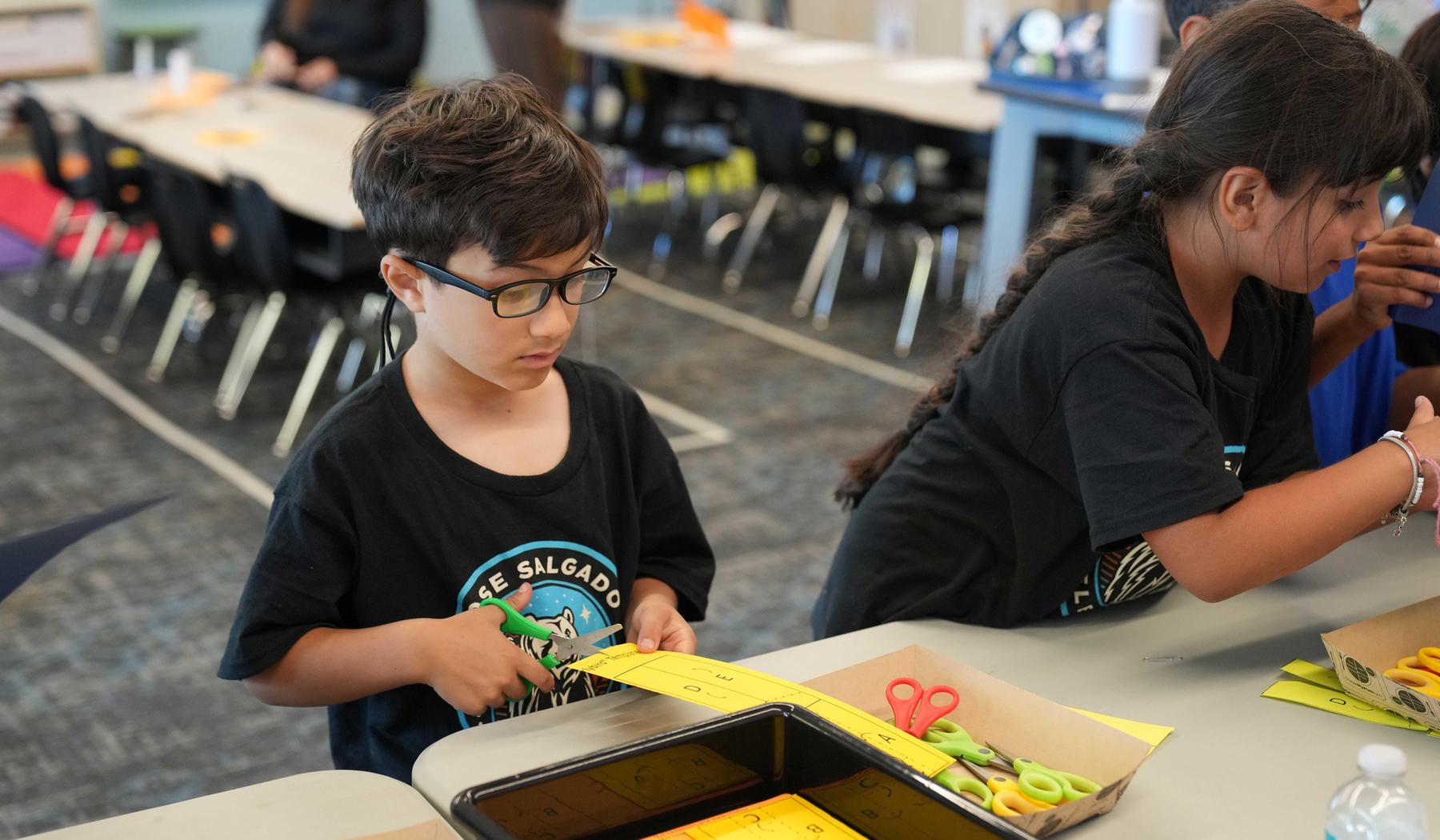 Boy standing at table cutting yellow paper