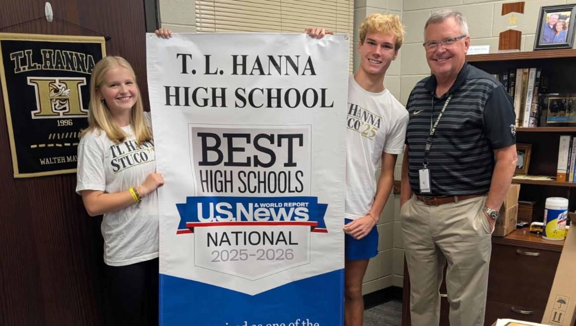 A group of two students and one adult holding a large banner that reads, "T.L. Hanna High School, Best High Schools, U.S. News & World Report, National 2025-2026." The banner also says, "Recognized as one of the 'Best High Schools' by U.S. News & World Report."