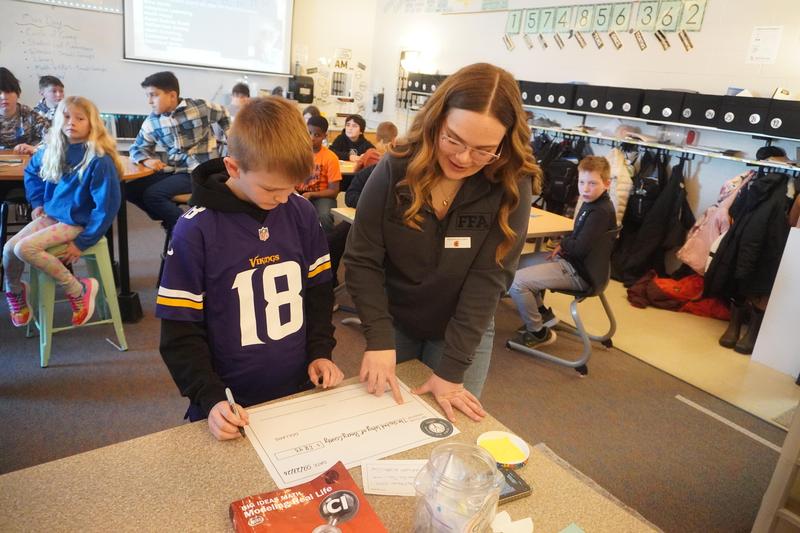 A high school YAC member helps a 5th grader fill out a large paper check to present to a local charity.