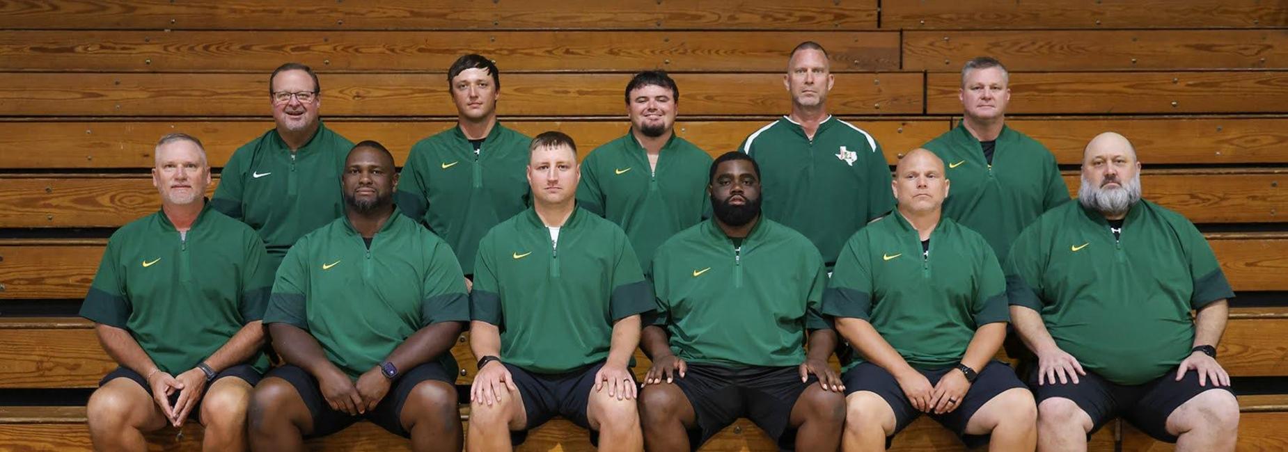 Group of coaches posing on bleachers wearing green athletic gear.