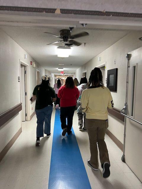 Individuals walking down a hallway with blue flooring.