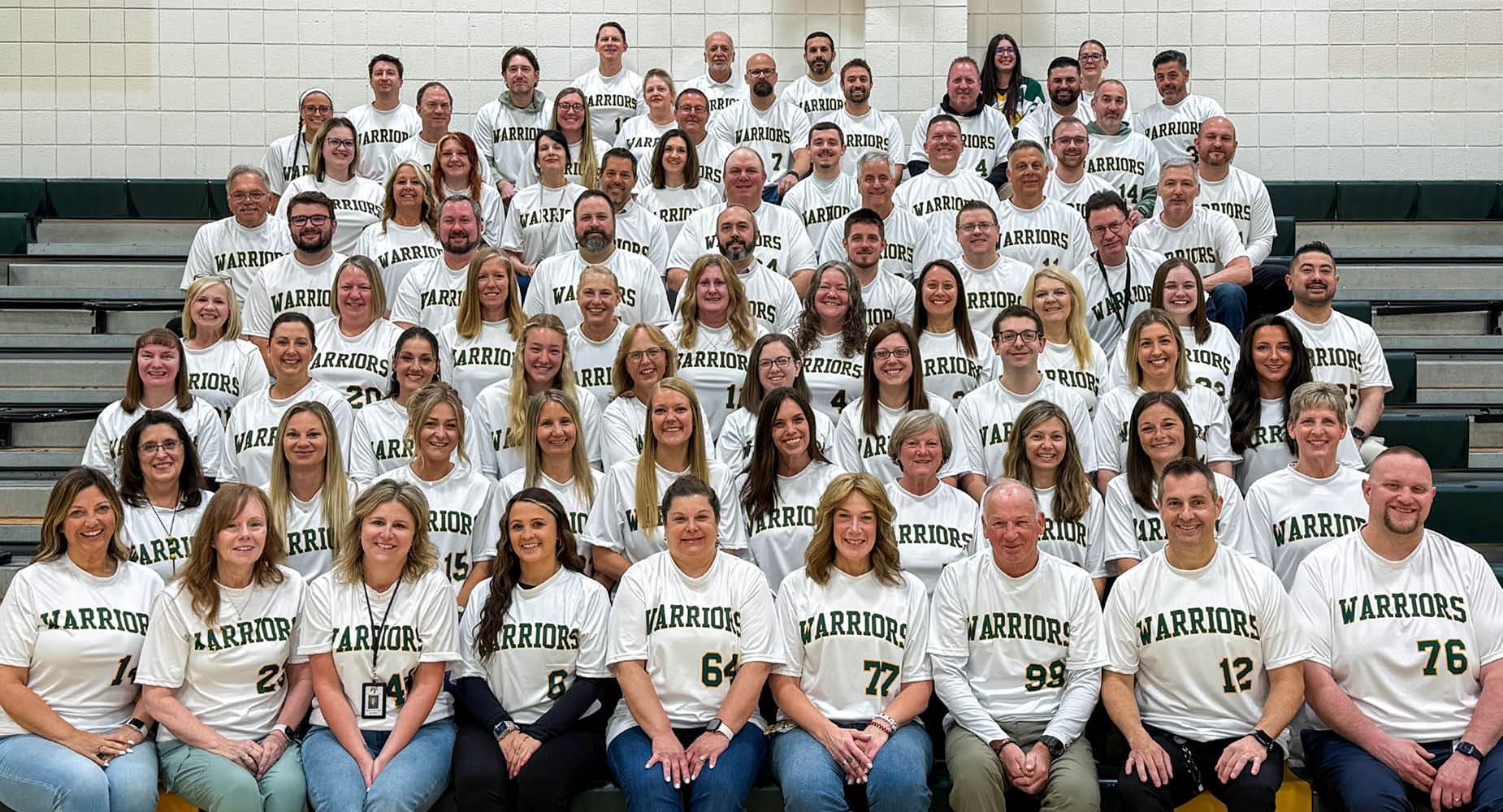 Group of High School teachers in matching shirts posing together in a gymnasium.