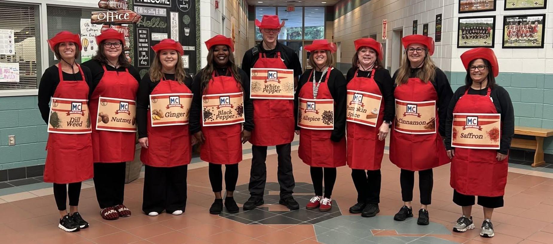 A group of people in red aprons and hats pose together in a school hallway.