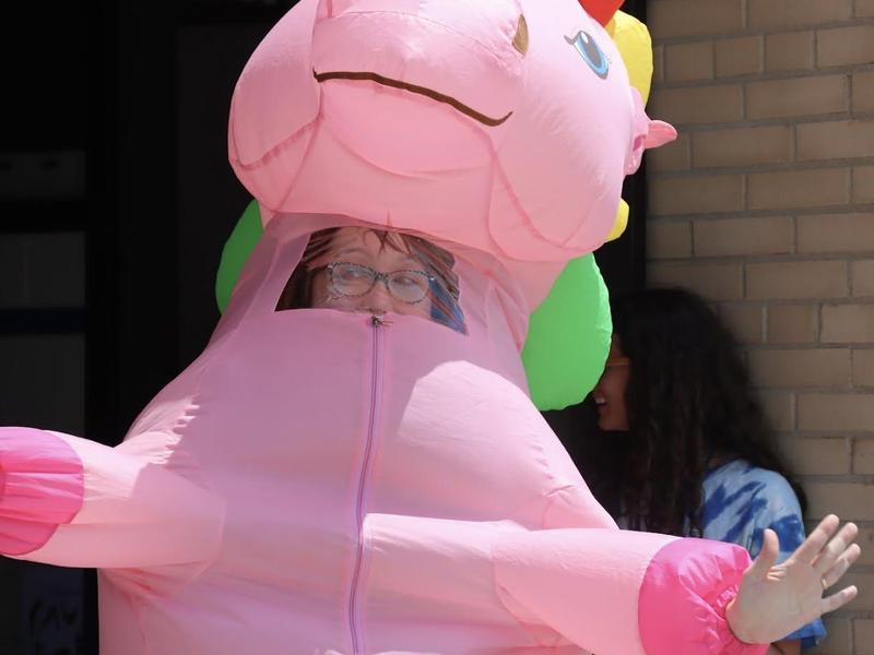 Person in a large pink unicorn costume smiles at the camera.
