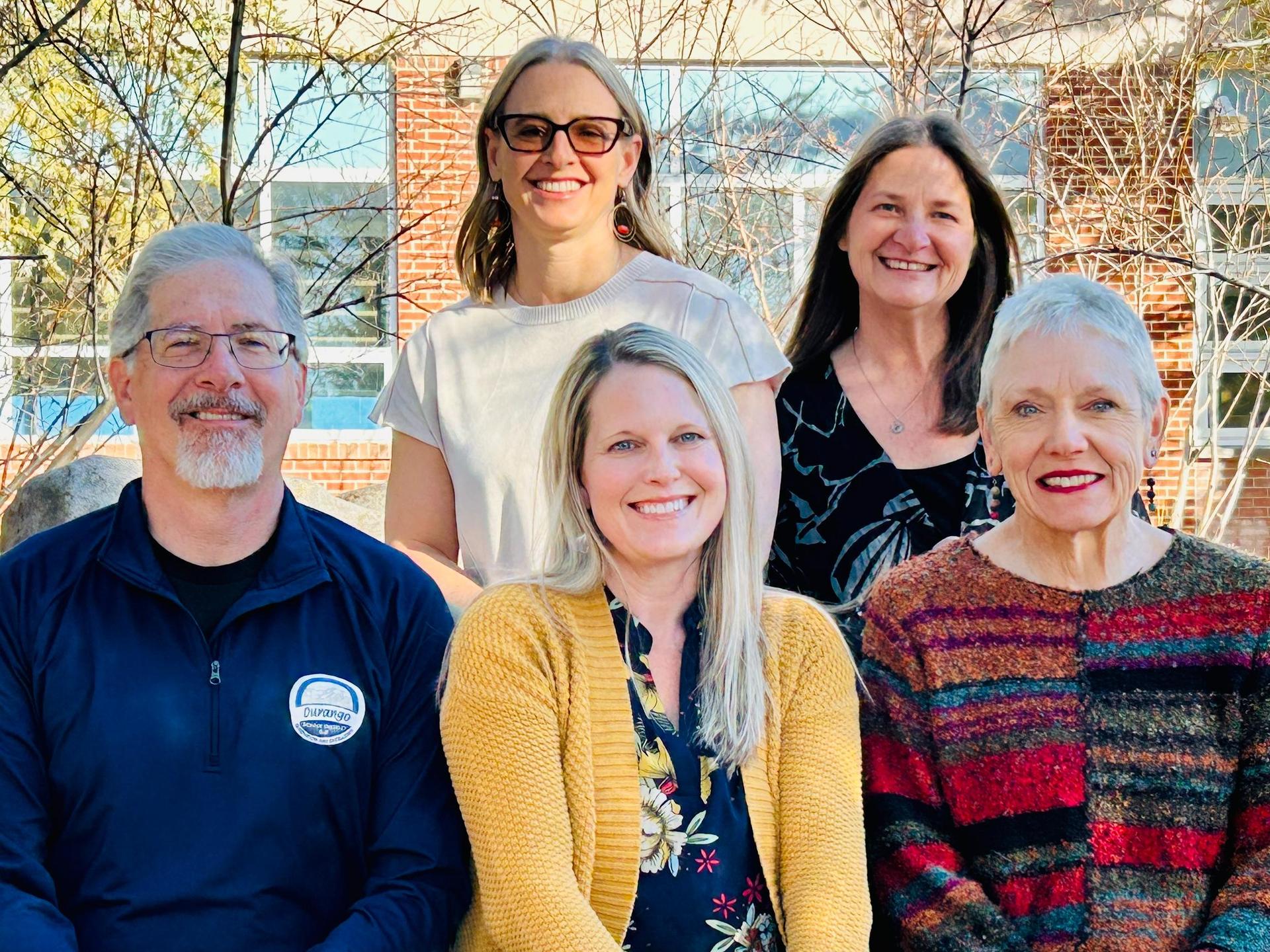 Five smiling adults seated in a school courtyard