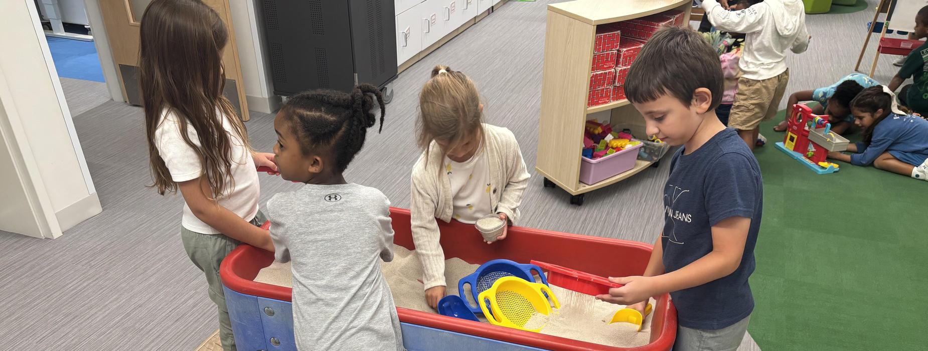 Preschool students working in the sand table and on the floor with toys.