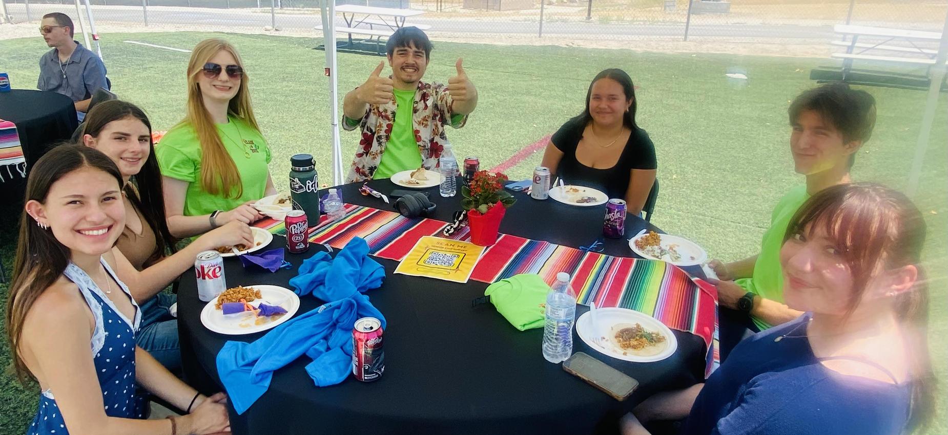 Group of six people enjoying a meal at a round table under a tent.