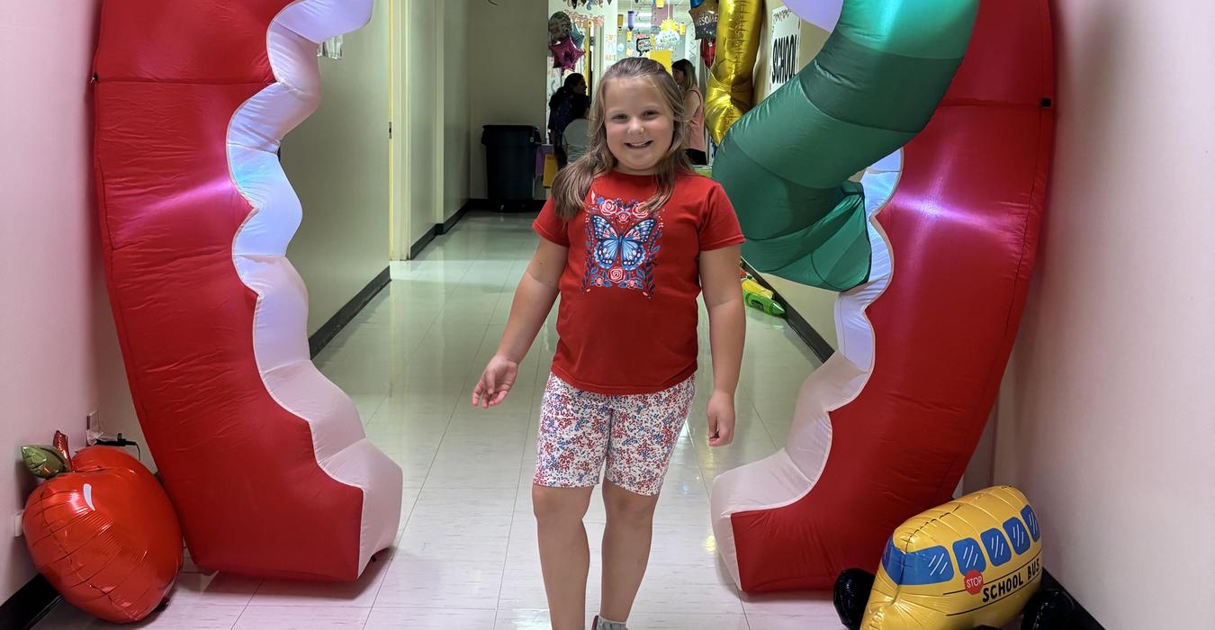 Child in a red shirt stands in a colorful inflatable archway in a hallway.