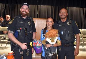 Two police officers with a student holding a plush lion at an event.