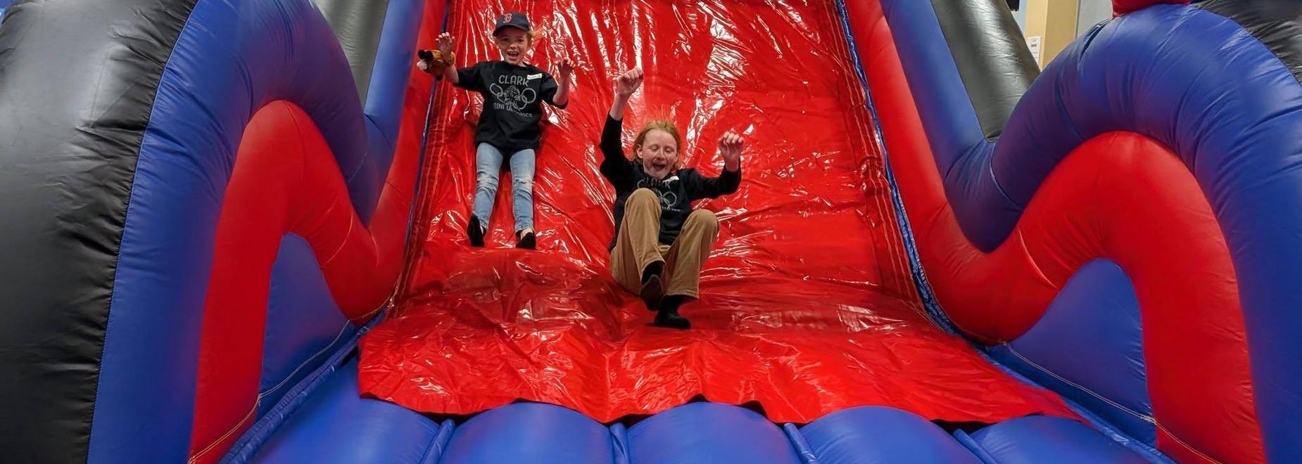 Two children joyfully sliding down a colorful inflatable slide.