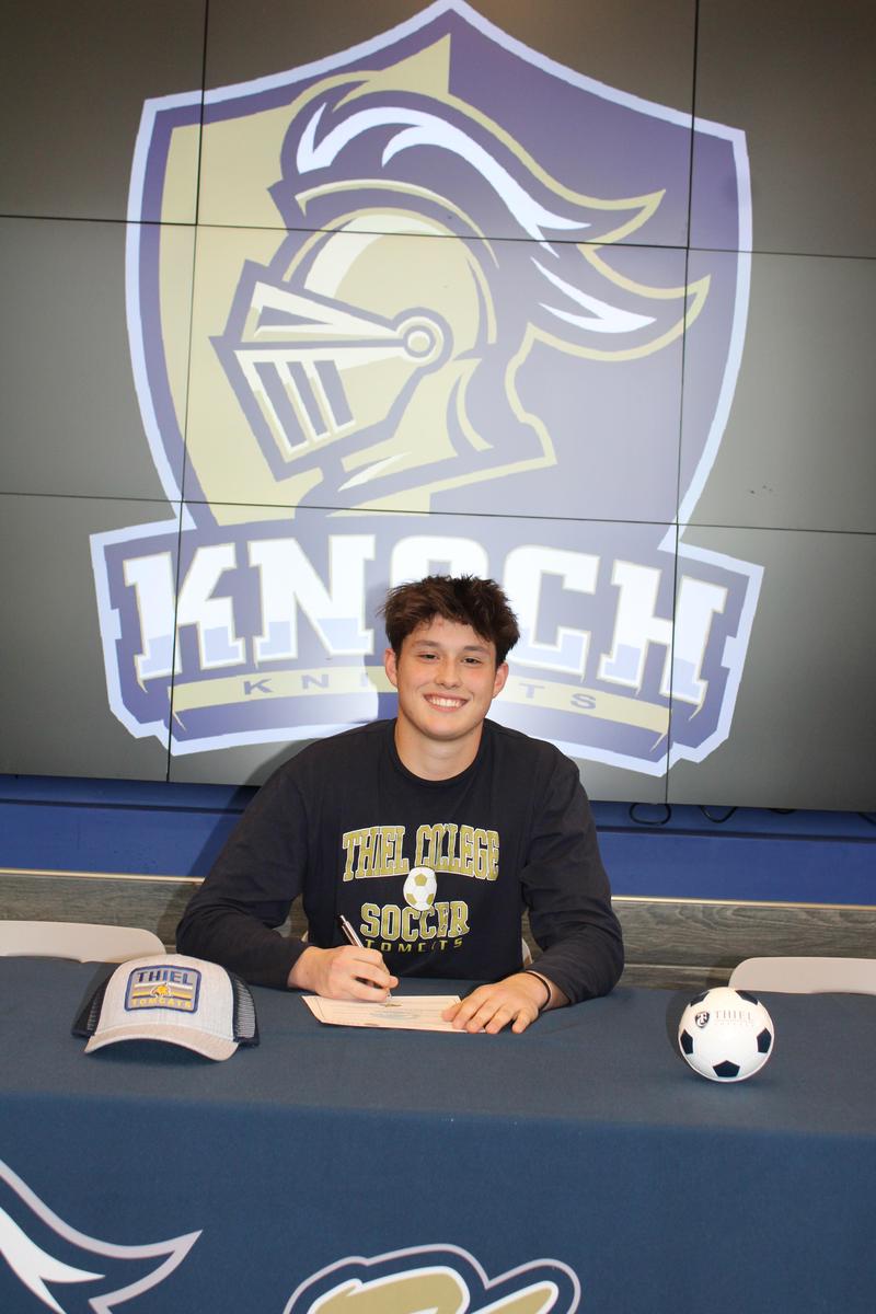 boy smiling with Knoch logo behind him and thiel college items on table