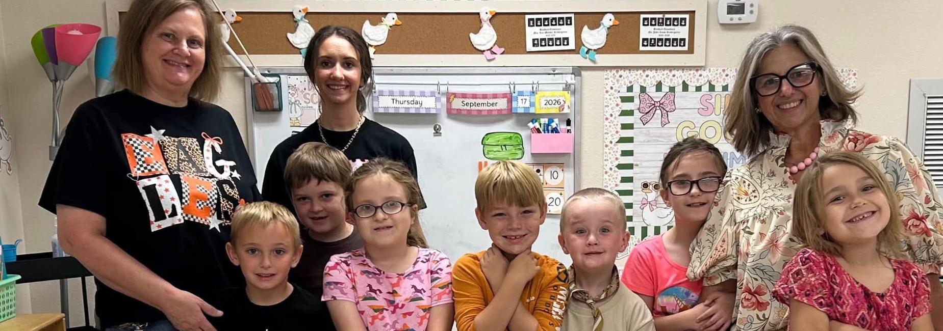 Group of children posing together with smiling faces in a classroom setting.
