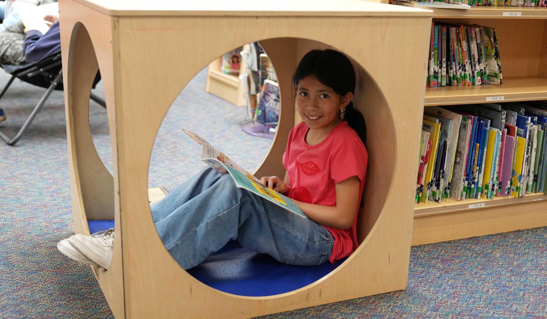 Child sitting inside a circular reading nook, enjoying a book.