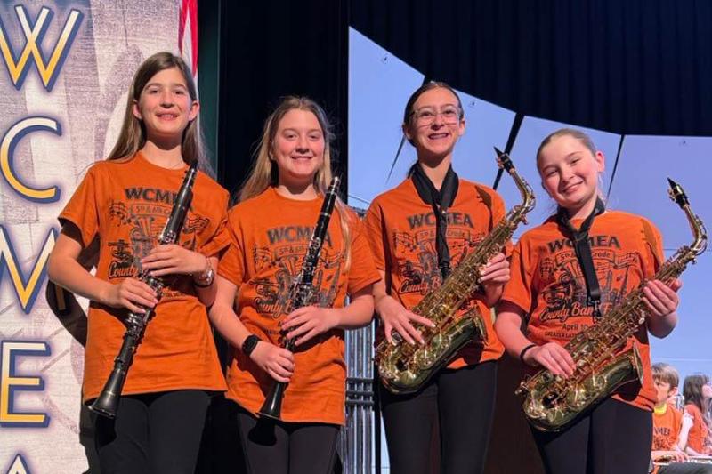 4 Penn Middle students are pictured holding their instruments and standing on the stage