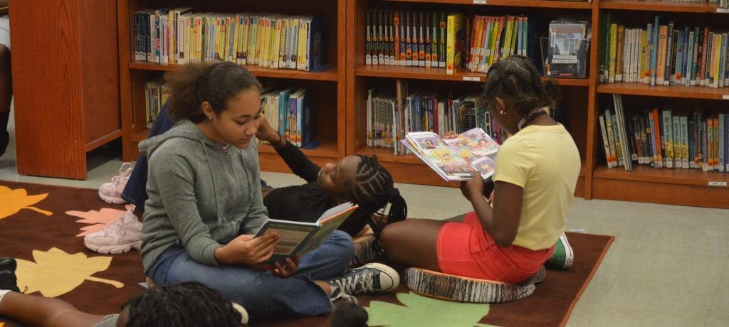 3 girls reading books on library rug