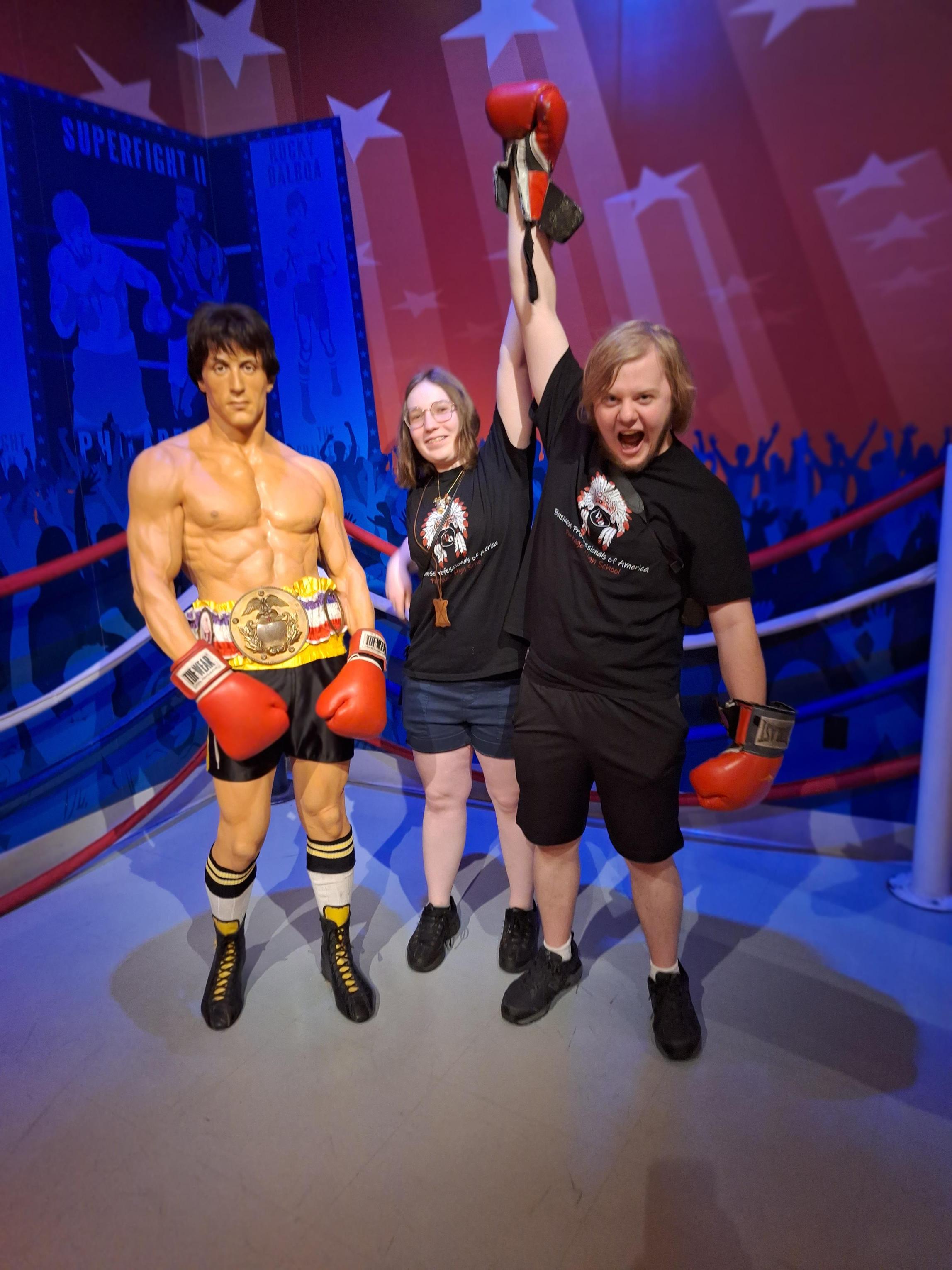 Two friends posing with a life-sized statue of a boxer, celebrating a win.