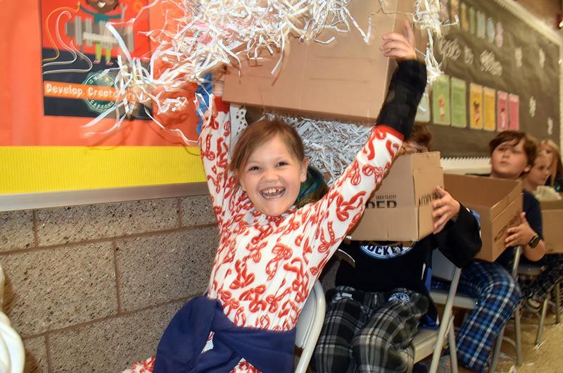 Child in festive pajamas joyfully holding up a box with shredded paper.