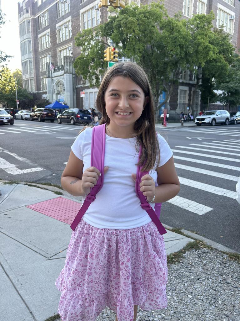 A girl standing across the street from the school on the1st day of school
