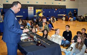 A speaker discussing items with a group of students sitting on the gym floor.