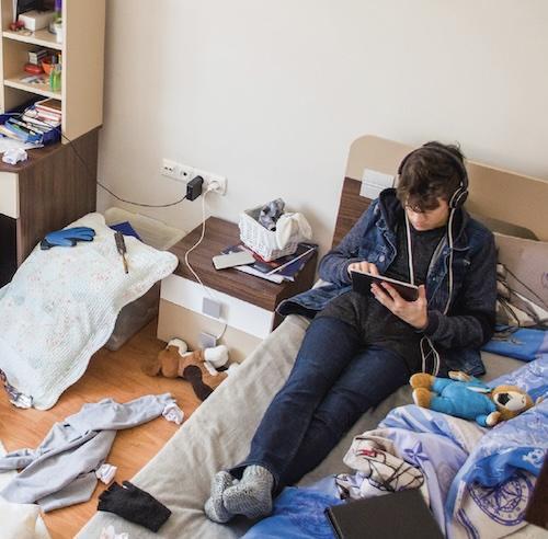 Teenager with headphones and tablet in a messy room