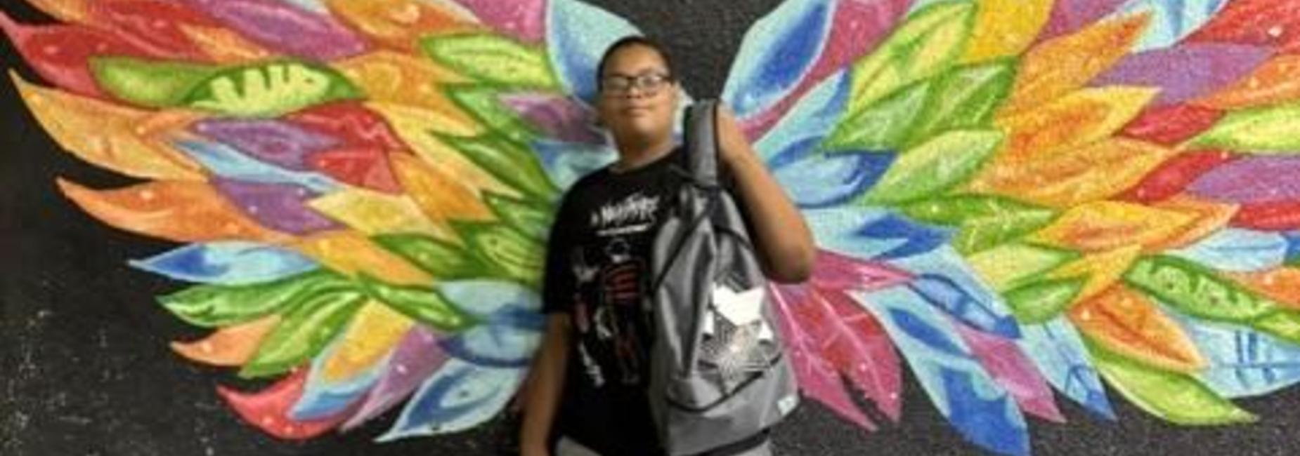 Student holding backpack behind wing painting