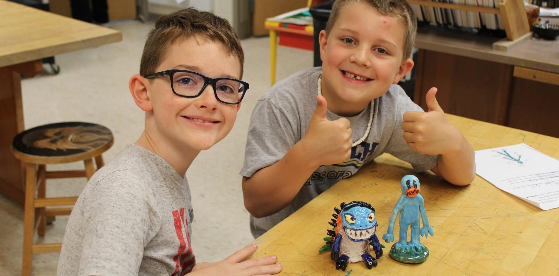 Two smiling boys pose with their colorful handmade creatures on a table.