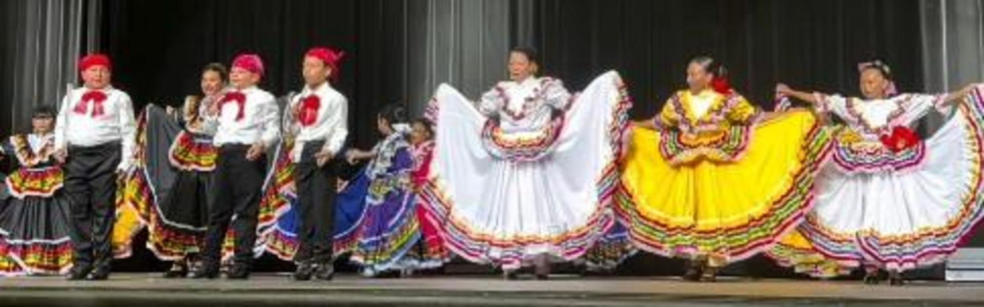 Group of children performing traditional dance in colorful costumes on stage.