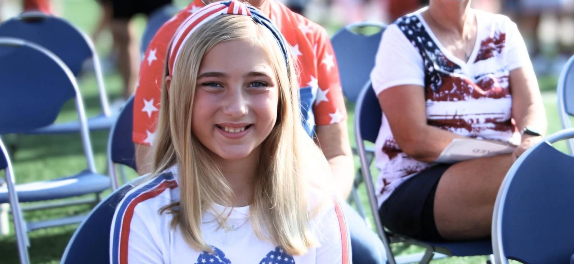 Girl with long hair smiling in a patriotic outfit at a gathering.
