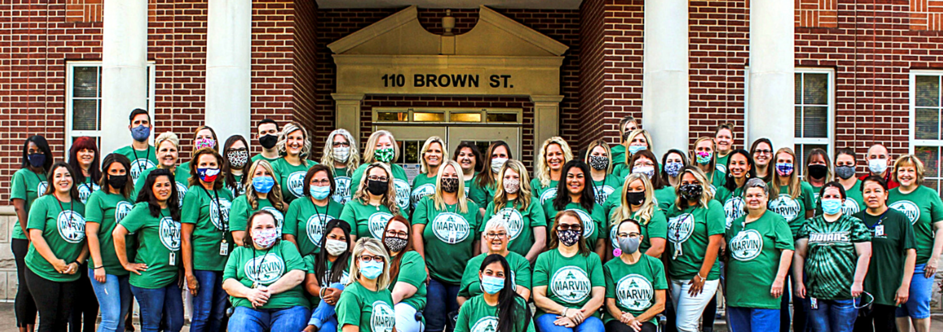 entire staff in matching shirts pose at campus entrance