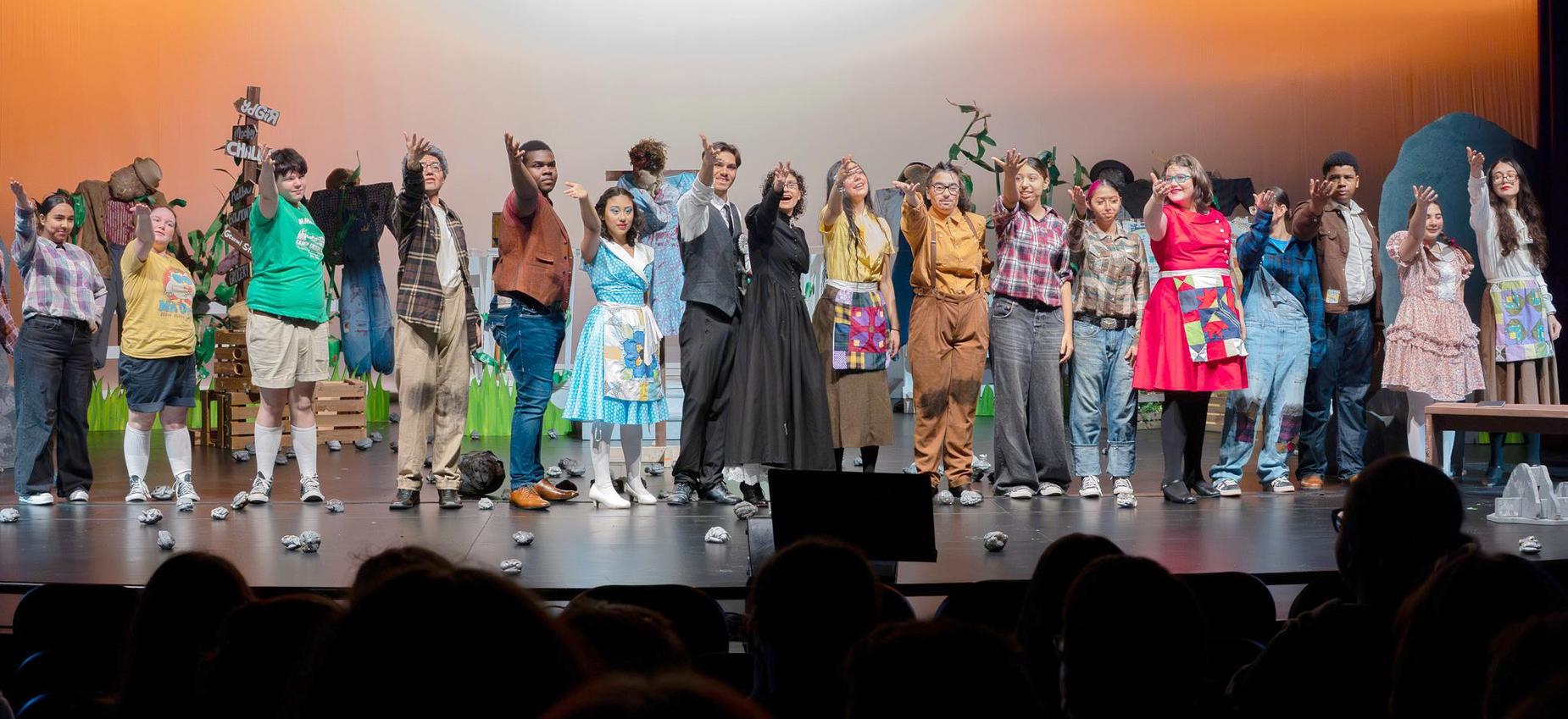 A diverse group of performers on stage, waving after a theater production.