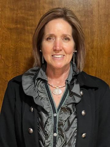 Woman in a ruffled gray blouse smiling against a wooden backdrop.