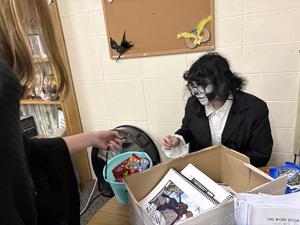 A student with face paint interacts with another student at a table.