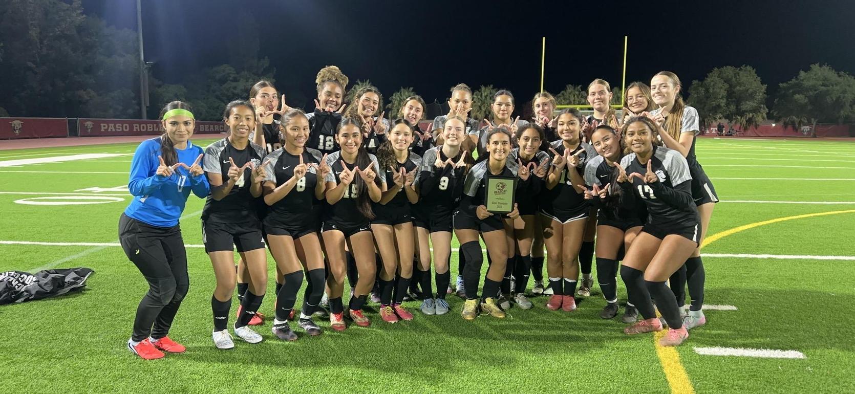 A team of soccer players celebrating with a plaque on the field at night.