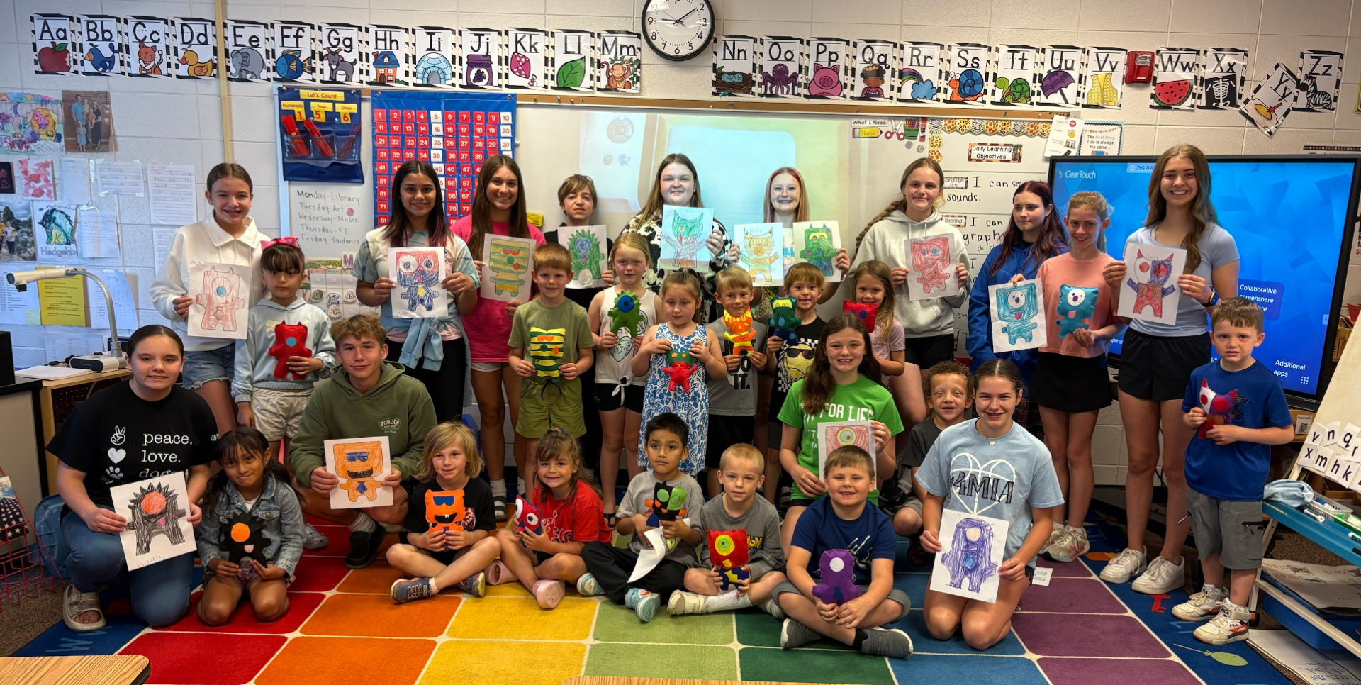 Large group of students showing art projects in a colorful classroom.
