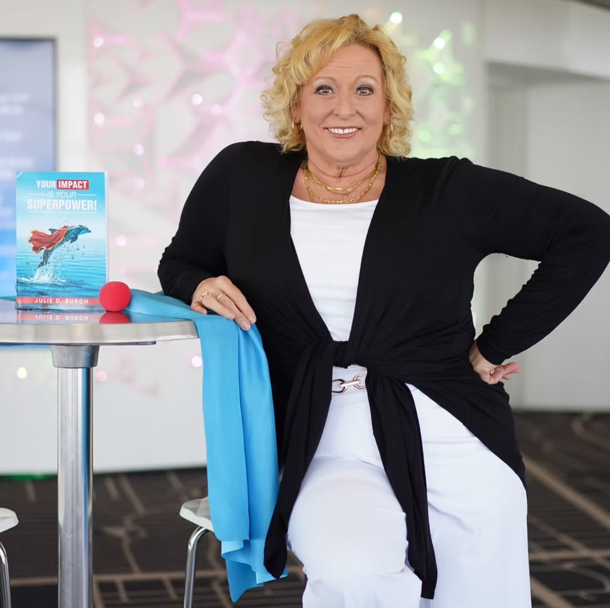 Julie Burch smiling, seated next to a table with a copy of her book