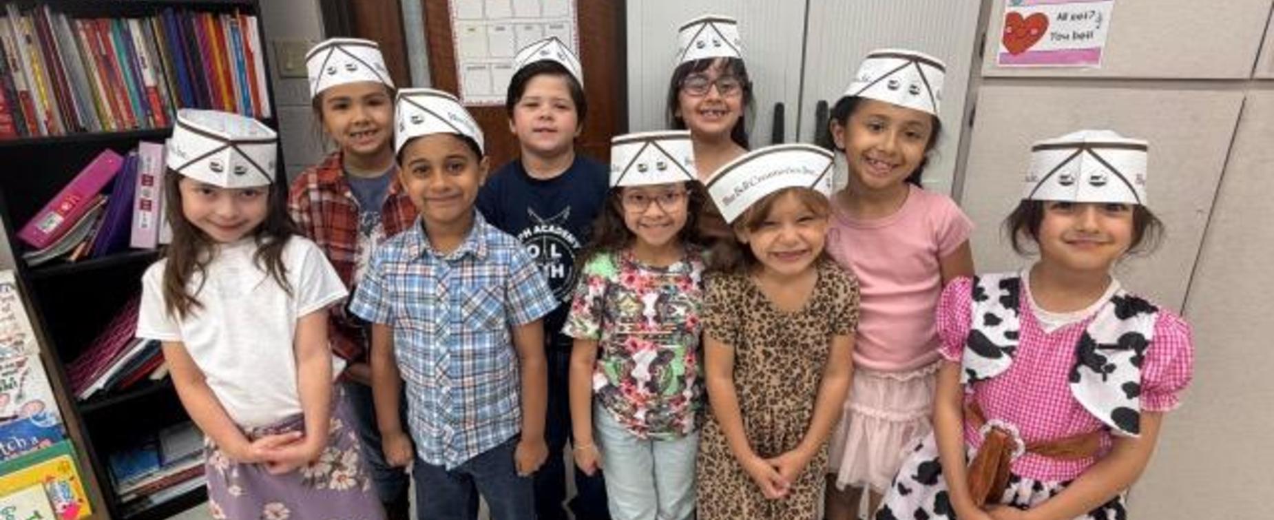 Group of children wearing paper hats, smiling together in a classroom.
