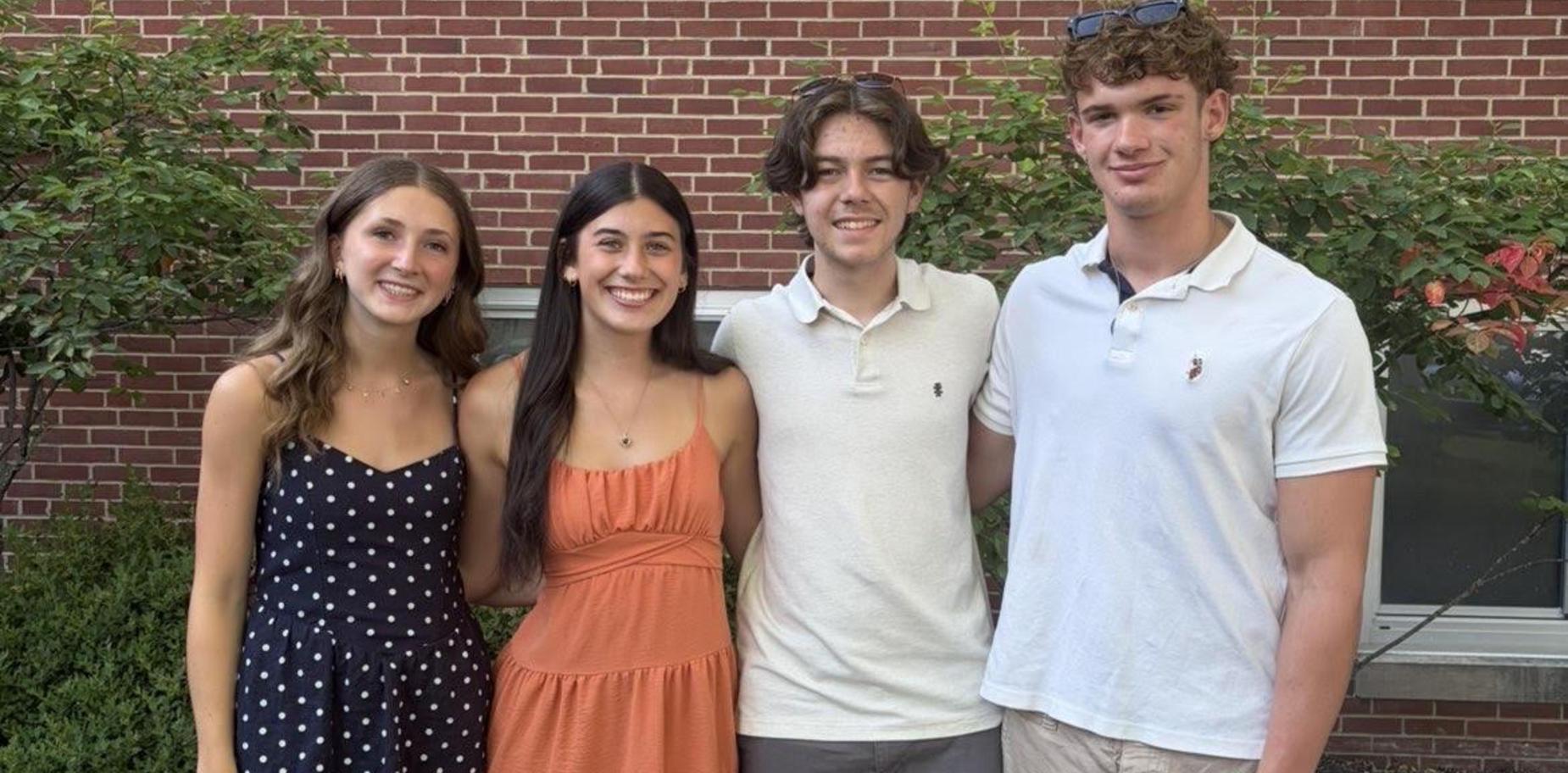 Four young adults posing together in front of a brick wall outdoors.